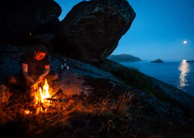 Making a bonfire in a cave close to the ocean in Norway. Moonlight reflecting on the sea.